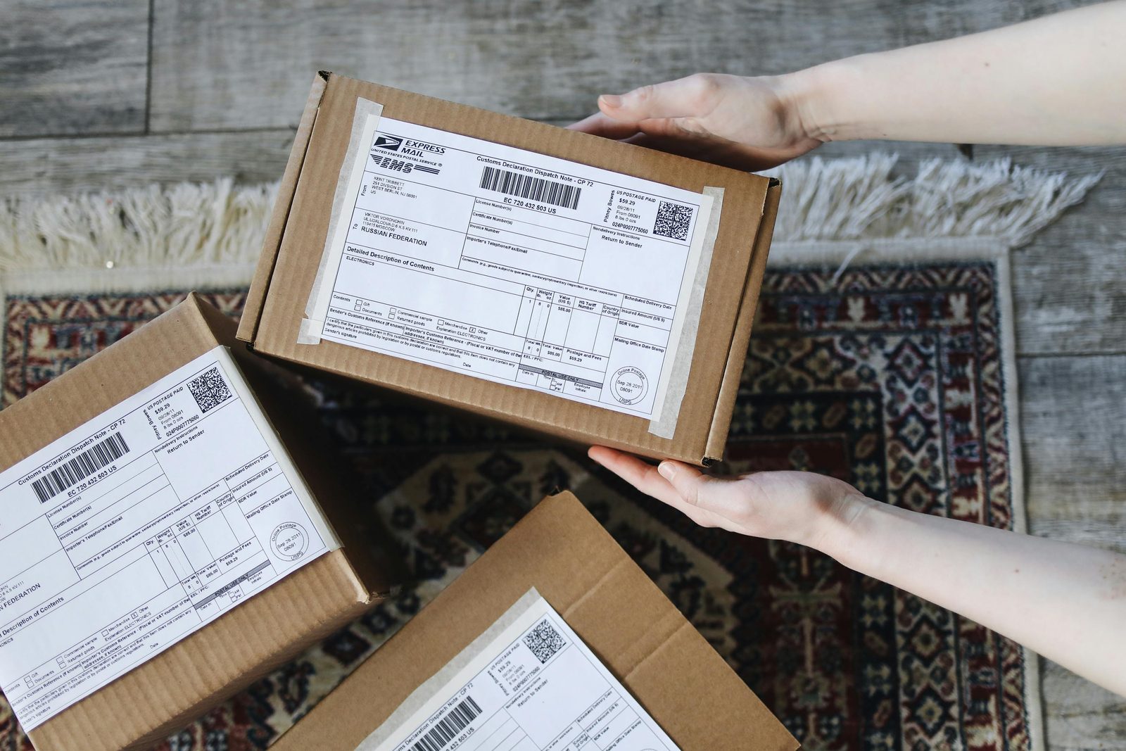 Hands holding cardboard parcels with printed shipping and customs labels