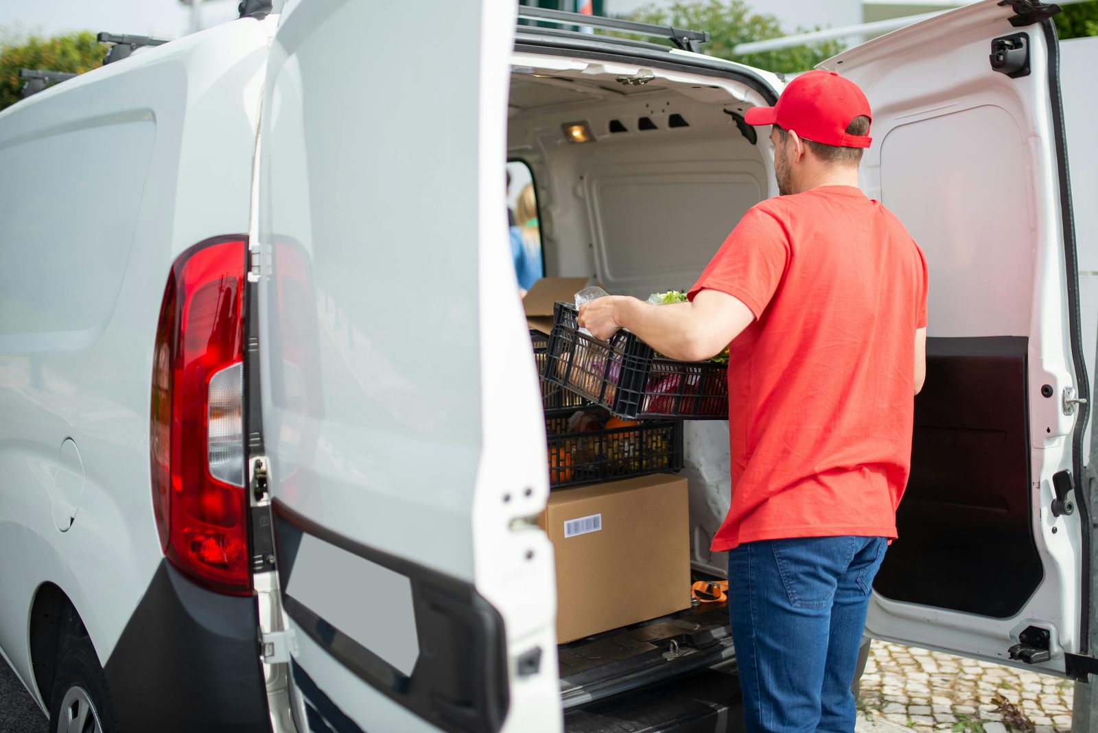 A delivery driver loading a crate of groceries into the back of a white van