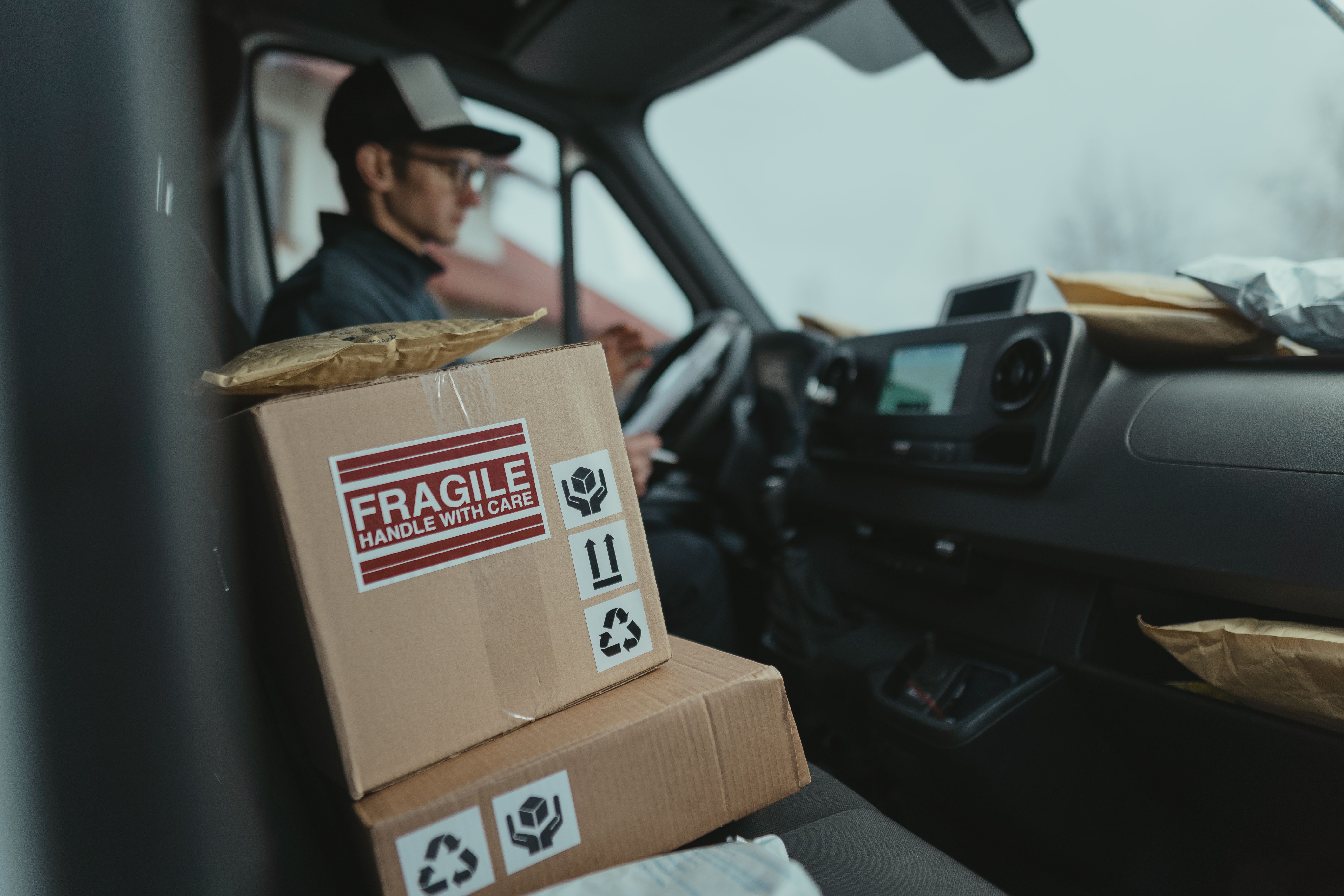 A delivery driver sits in a van cab with parcels marked Fragile on the passenger seat.