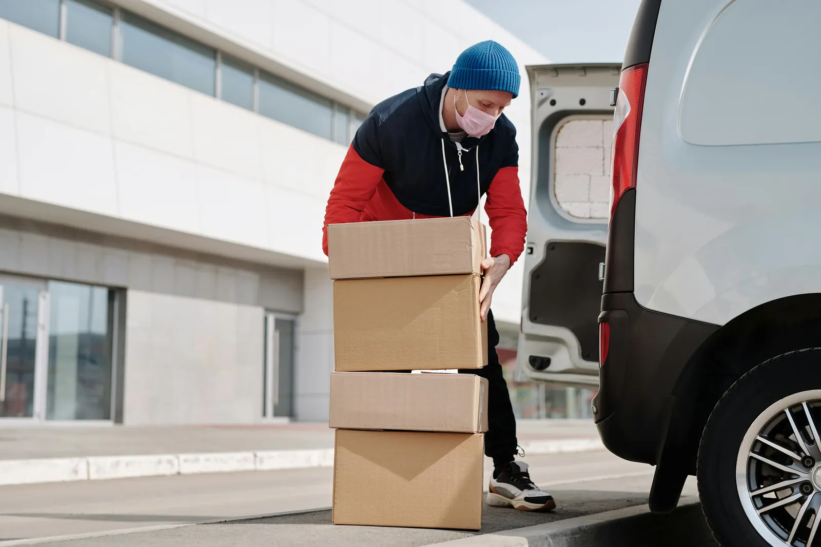 A delivery driver stacking cardboard boxes beside the open back door of a white van