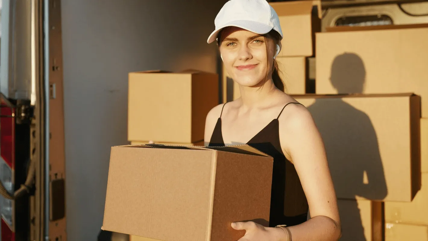 A delivery worker holding a cardboard box in front of a loaded van