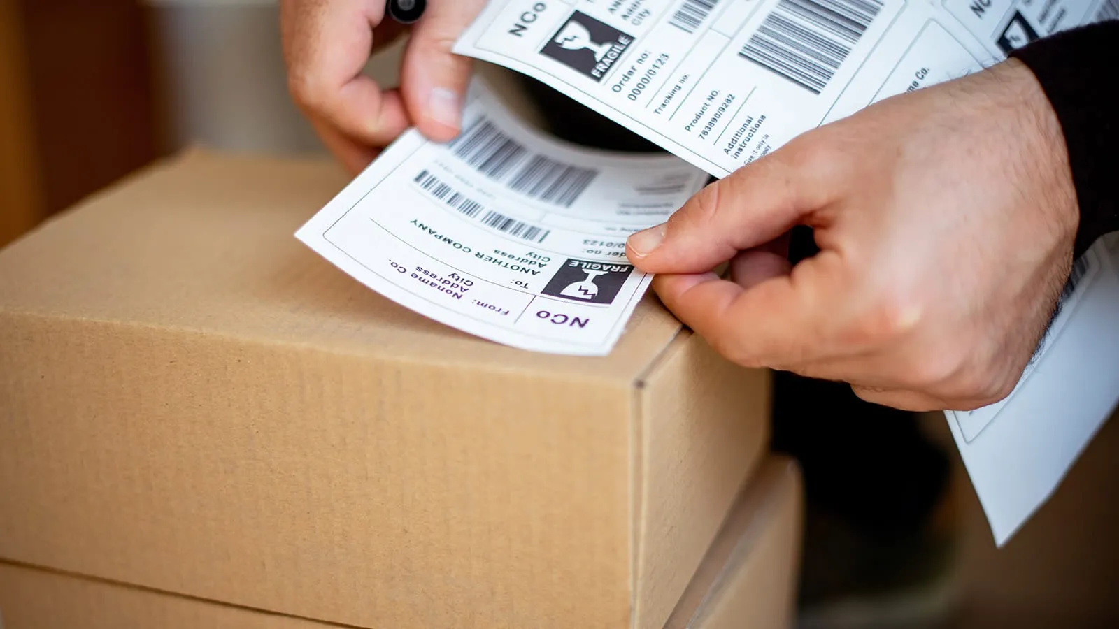 Hands applying a shipping label to a cardboard box