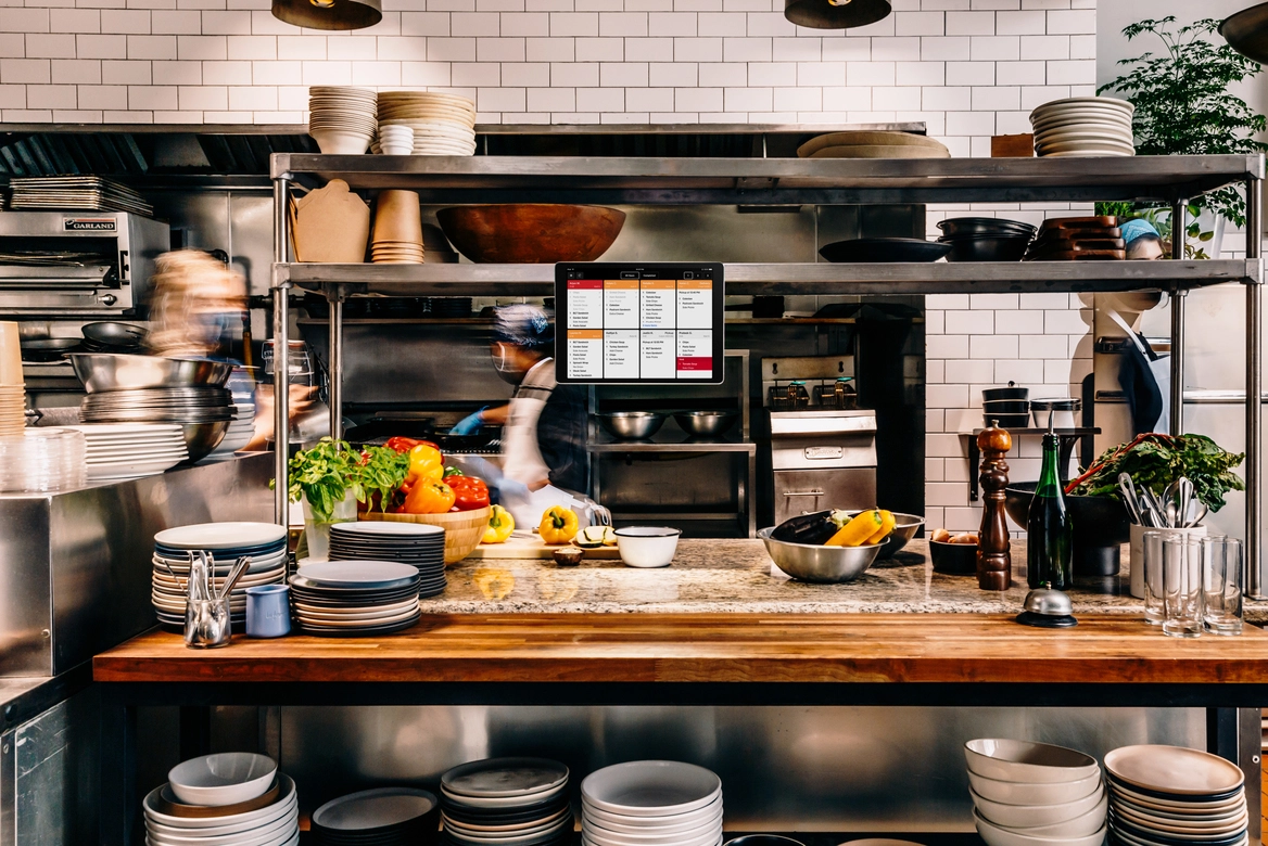 A busy commercial kitchen with prep counters and an order screen
